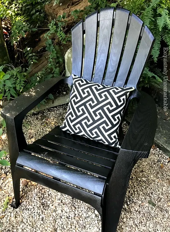 Black Adirondack chair with white and black pillow on gravel patio