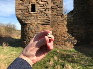 View of a hand holding Skulferatu #26, with part of the tower of Saltcoats Castle in the background.  Photo by Kevin Nosferatu for the Skulferatu Project.