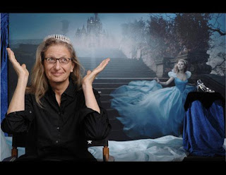 Image: Annie Leibovitz, a 61-year-old, bespecled woman with a prominent nose, sits in a directors chair wearing a 62-carat, diamond tiara. Her palms are pointed to the heavens, as if to say "all done!&quote; To her left, on a draped pedestal, there is a high-heeled, glass slipper.
Behind them both, Actress Scarlett Johansen runs hurriedly down an old-style garden staircase; looking around for her carriage to escape from the Disney World castle. She wears the same tiara and her ball gown flows behind her, up the steps. On the landing behind her, the same glass slipper can be seen, highlighted by a spotlight. Caption: 