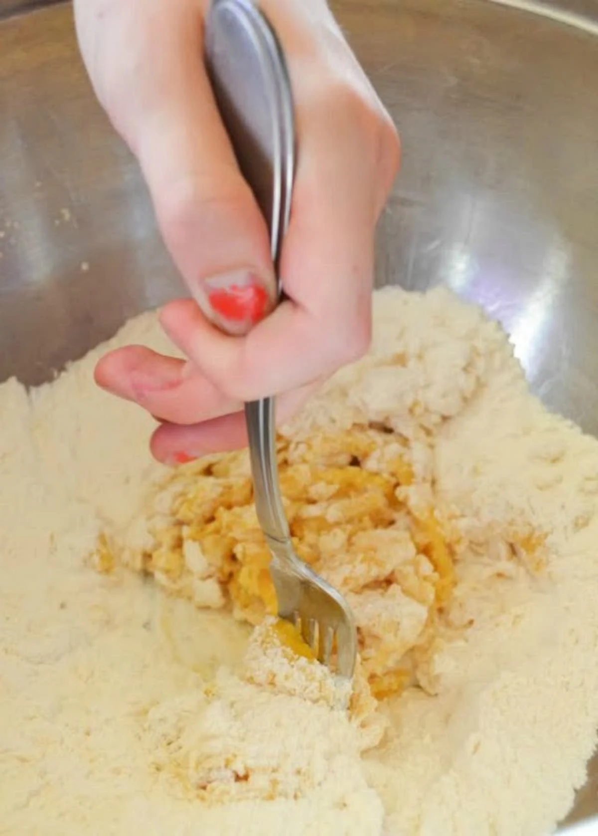Egg and Vanilla being stirred in with flour in a mixing bowl using a fork.