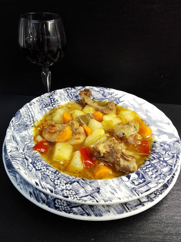 Plato de caldereta de conejo con patatas y copa de vino tinto.