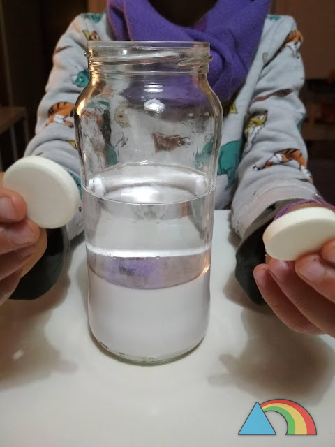 Bote de cristal con agua tintada de blanco y aceite mineral. Preparadas dos pasillas de vitamina C para empezar la tormenta de nieve en un frasco