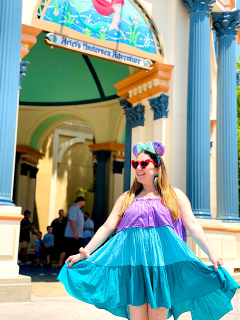 Jamie Allison Sanders smiling and holding out her striped dress in front of Ariel's Undersea Adventure at California Adventure.