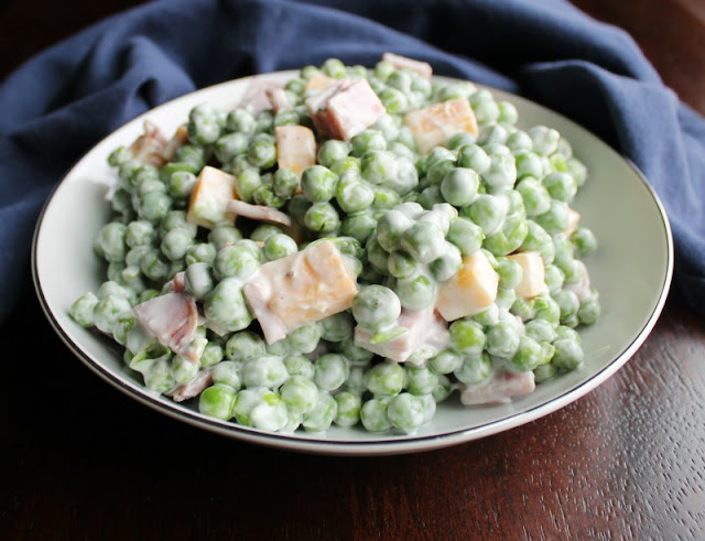 Perfect for a picnic, or Easter or any time! This pea salad is made with yogurt instead of mayo which makes it lighter and fresher! A little ham and cheese never hurt anything either! close up of a serving bowl of lightened up pea salad with cheese and ham
