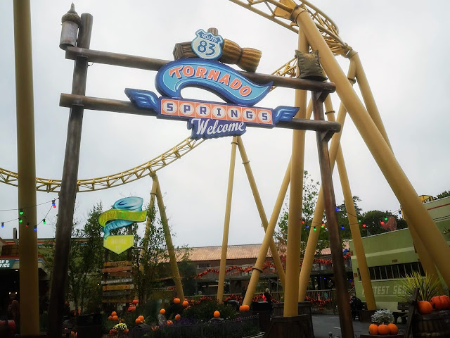 Image of the entrance to the Tornado Springs American themed part of the theme park. The image shows the Tornado Springs sign and the looping tracks of the Storm Chaser rollercoaster.