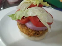 Arranging burger patty,onion tomato slice and lettuce over burger bun for veg burger recipe