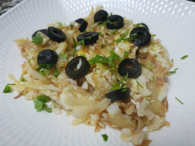 Bacalao con patatas paja y cebolla, adornado con perejil y aceitunas negras