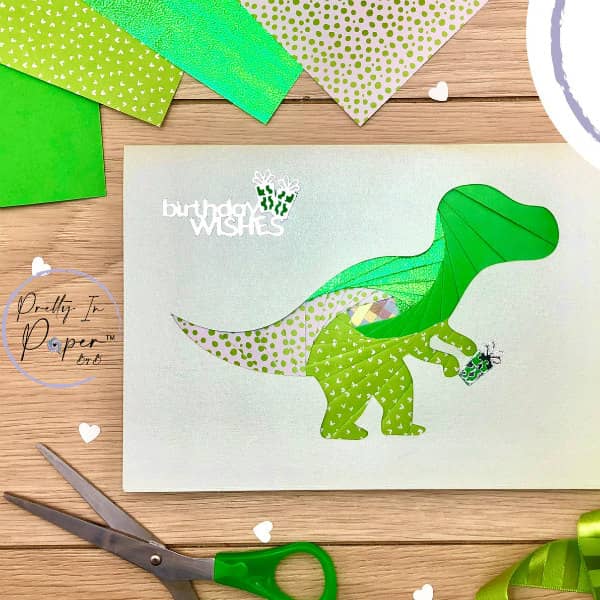 iris gevouwen dinosaurus verjaardagskaart op tafel omringd door papieren knutselspullen