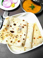 Serving folded rumali roti with curry, onion slice in background