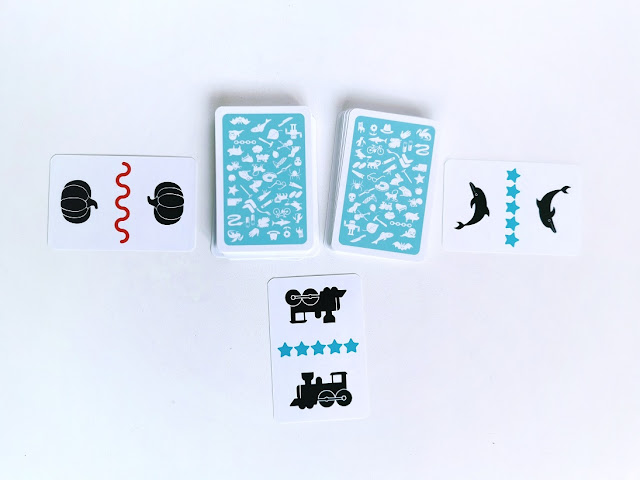Gra słowna Na końcu języka , na srodku stołu lezy talia niebieskich kart w dwóch zakrytych stosach, wokół rozlożone sa trzy odkryte kart, dwie z nich maja ten sam wzorek