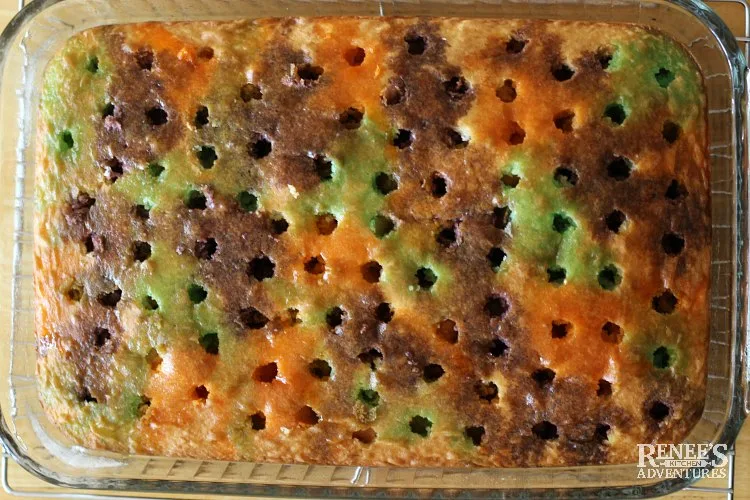 Process image of Halloween Jello Poke Cake by Renee's Kitchen Adventures  over head view of cake poked with holes and gelatin poured over it in alternating colors and flavors