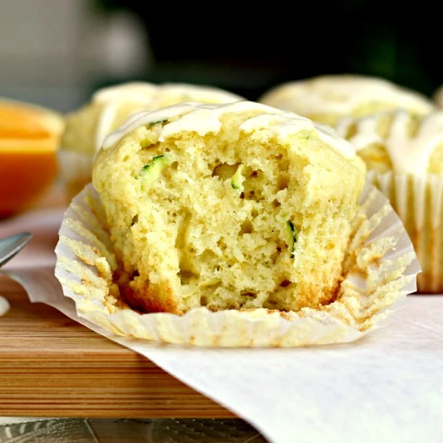 Glazed Orange Zucchini Muffins by Renee's Kitchen Adventures muffin on board with bite taken out so you can see flecks of zucchini inside and tender crumb