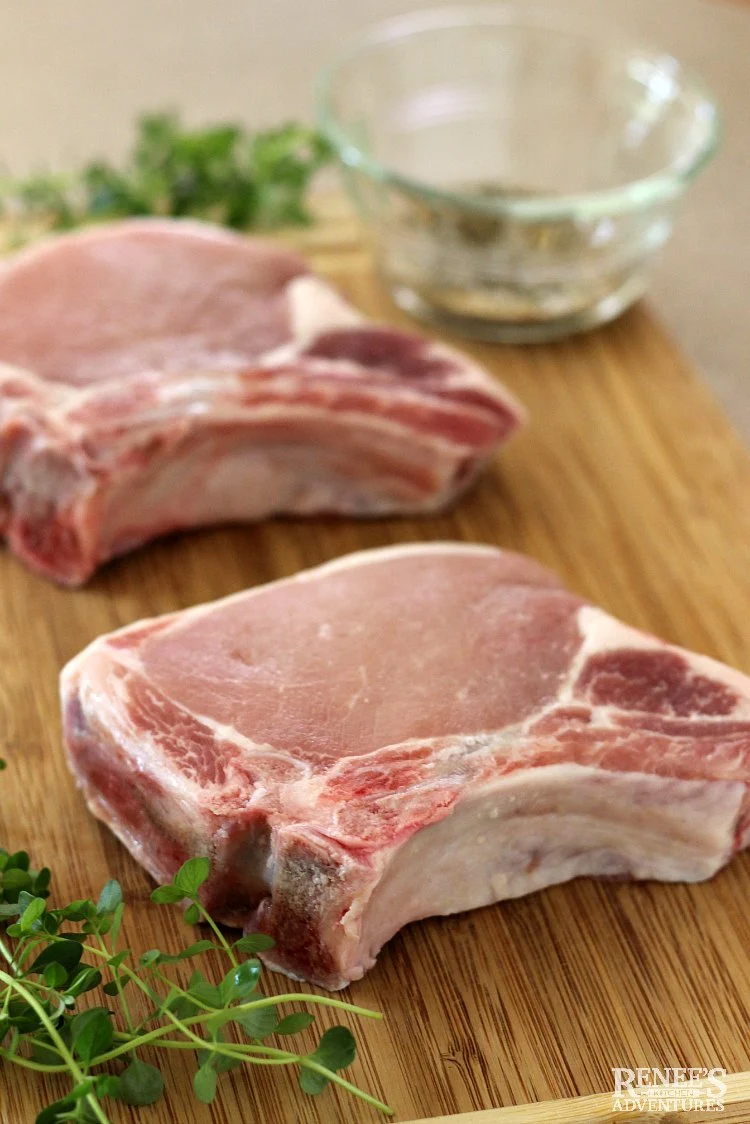 Thick cut bone in pork chops on board, raw and ready for seasoning