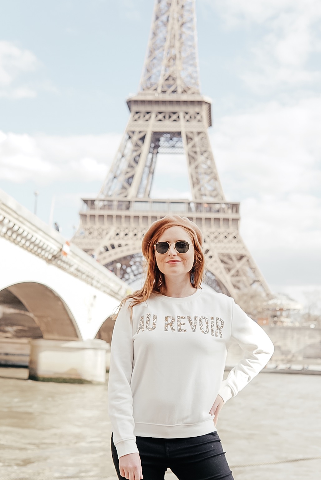 tampa blogger amanda burrows of affordable by amanda wears a white "au revior" sweater from h&m standing in front of the Eiffel Tower.