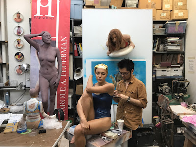 An artist applies hairs to a mannequin in a space crowded with in-process pieces.