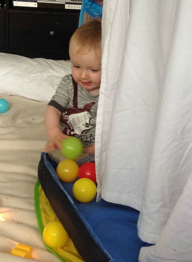 baby playing with coloured balls inside a den made with a sheet