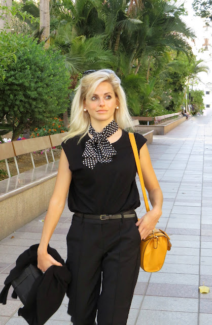 Alejandra Colomera con camiseta negra, pantalón formal negro, lazo en el cuello negro con lunares blancos y complementos mostaza