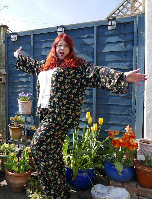 A red-haired woman in a flowery jacket and trousers. She is posing with both arms out and saying "WAHEY!"