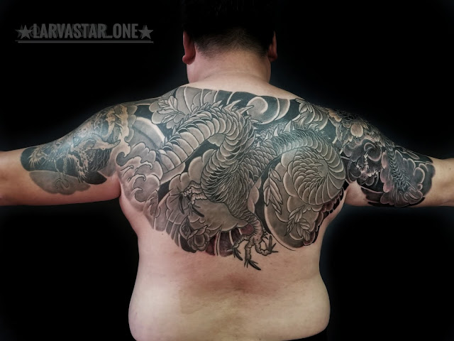 man with open arms showing a back piece in black and gray Japanese  style dragon tattoo with waves crashing , black clouds and peony leaves