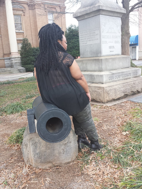 Plus size blogger reflecting on times of old, wearing army fatigue, black blouse, and stacked booties.