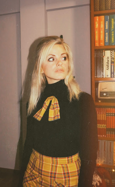 Alejandra Colomera con falda de cuadros mostaza, lazada a juego, jersey negro y abrigo estilo sesentero