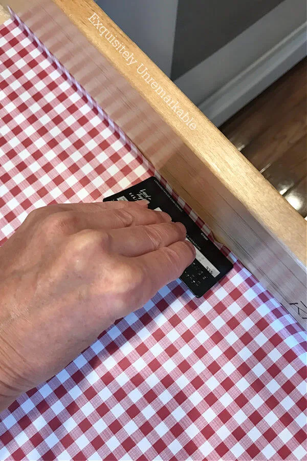 Using a credit card to smooth out red checked contact paper in a drawer