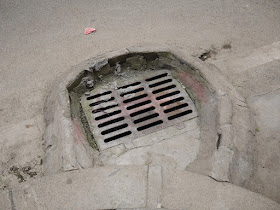 metal grating of a storm drain surrounded by a concrete wall