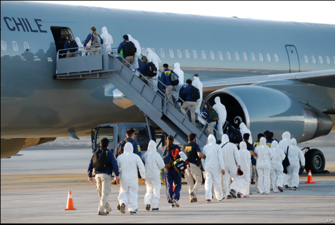 Migrantes venezolanos y colombianos que son deportados usan equipo de protección mientras caminan en línea con la policía para abordar un avión en el Aeropuerto Internacional General Diego Aracena Aguilar en Iquique, el 10 de febrero de 2021 / AP