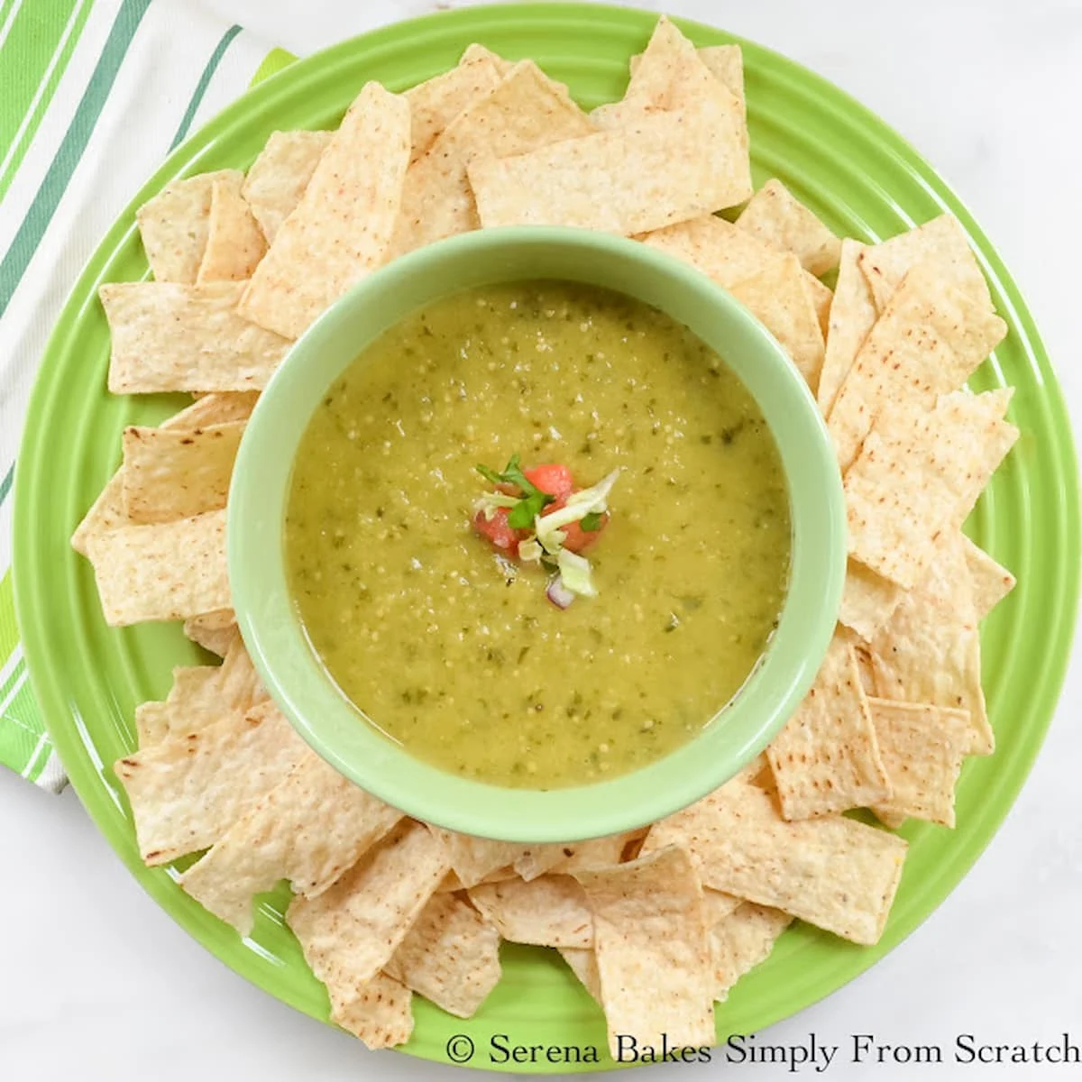 A green bowl filled with Salsa Verde and Corn Chips spread around the edge of a plate looking down.