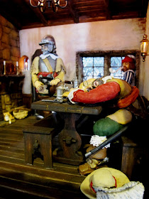 A man asleep at a table inside a one-twelfth scale miniature mid 17th-century inn.