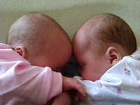 newborn twins sleeping on nursing pillow with foreheads touching