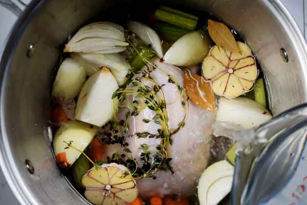 Adding water to stock pot with homemade chicken broth ingredients for how to make chicken broth