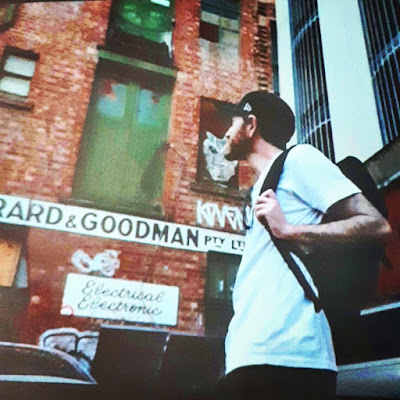Film image of artist Joshua Smith in the street, looking at the facade of an old building.