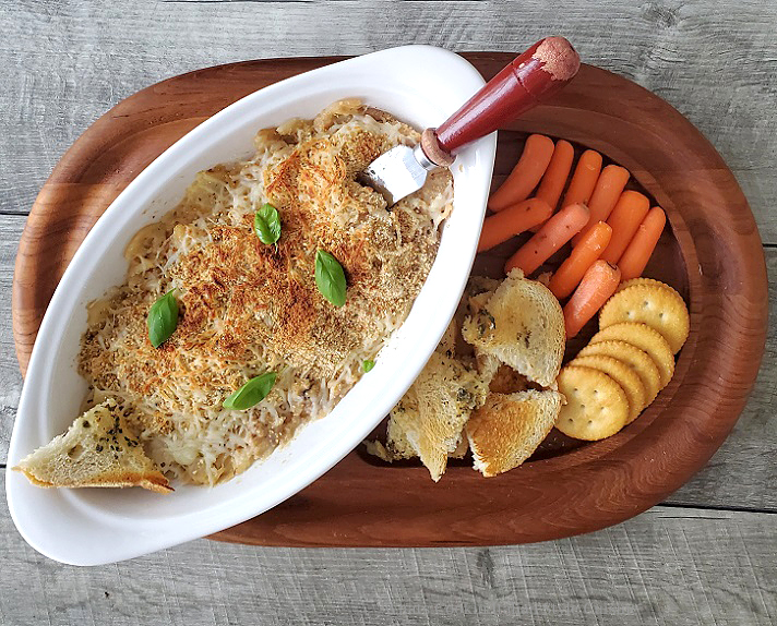Hot Crab Dip this is a hot crab dip on a wooden cutting board filled with assorted crackers, vegetables and garlic bread to dip into this hot crab dip