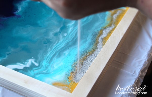 Pour handfuls of beach sand on the resin ocean paint pour.