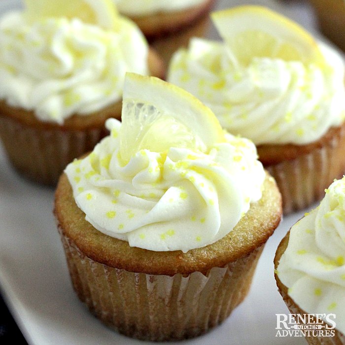 Easy Lemon Cupcakes by Renee's Kitchen Adventures on a white platter, garnished with lemon wedges and yellow sanding sugar close up