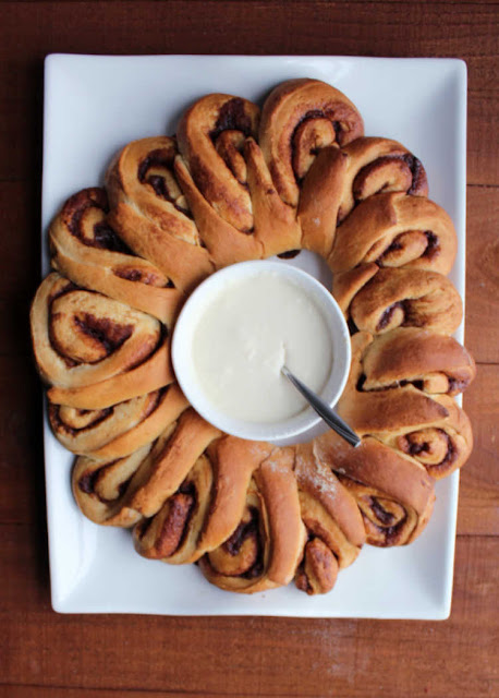 Soft and sweet cinnamon rolls take on a festive wreath shape. They are a perfect holiday breakfast or something fabulous for overnight guests. freshly baked cinnamon roll wreath with bowl of icing in the middle
