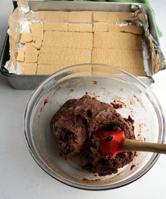 bowl of chocolate cake mix mixture with pan lined with graham crackers in background