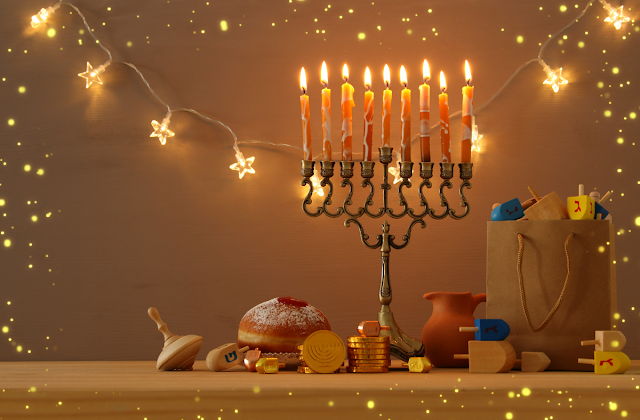 Photograph of a chanukah menorah on a table, surrounded by dreidels, gelt, and jelly donuts