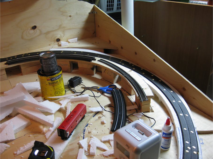 Benchwork covered in various construction materials as foam roadbed is applied and held in place with thumb tacks