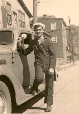 Young man in sailor's uniform leaning on car, circa 1943.
