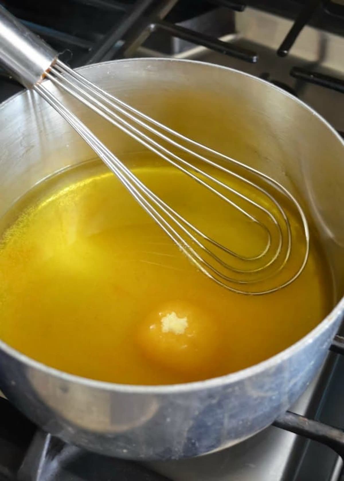 Lemon Jello being whisked into boiling water in a large saucepan.