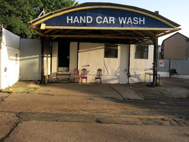 Chairs under a blue canopy announcing Hand Car Wash with concrete forecourt.