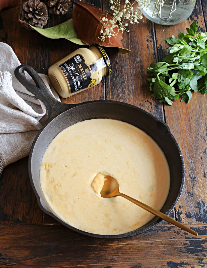 Recipe for browned ground beef cooked in a cheesy mustard bechamel sauce and served over baked potatoes.