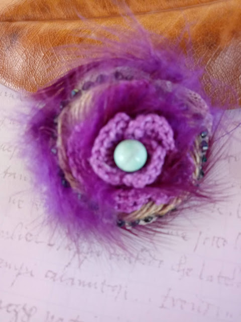 Flor hecha de ganchillo lila, cinta de yute, cuentas de color turquesa y plumas violeta