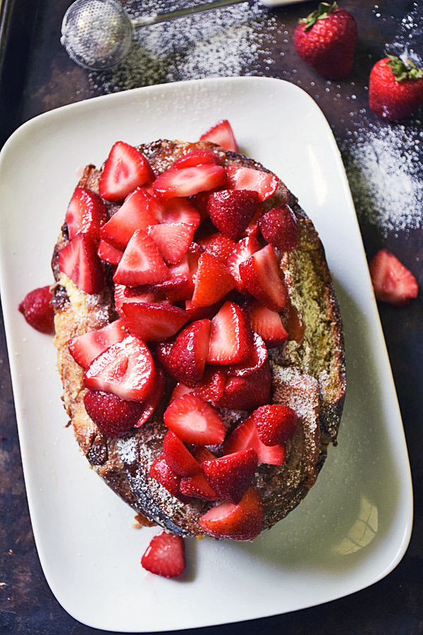 Loaf of slow cooker stuffed french toast on a white tray topped with sliced, fresh strawberries
