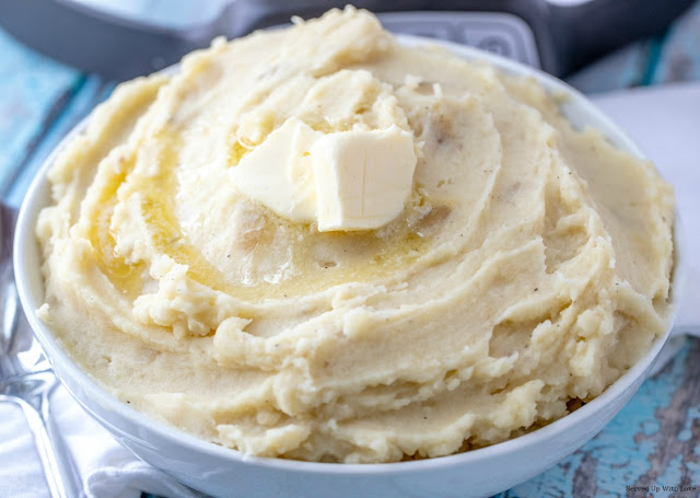 Bowl of creamy mashed potatoes with a slice of butter on top in white bowl