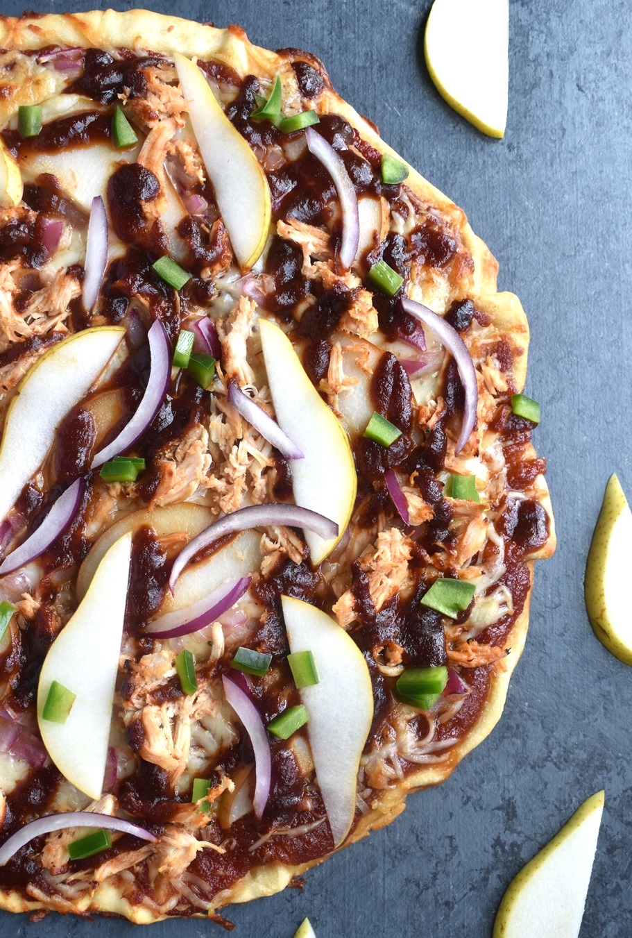 Pear BBQ Chicken Pizza features a thin crispy pizza crust topped with sweet and smoky barbecue sauce, shredded chicken, red onion, sliced pear, green pepper and melted cheese!
