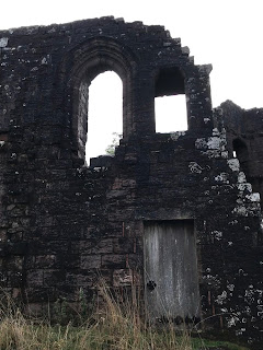 A photo of a wooden doorway and a ruined wall with two empty windows above the door.  This is one of the outer walls of Morton Castle.  Photograph by Kevin Nosferatu for the Skulferatu Project.