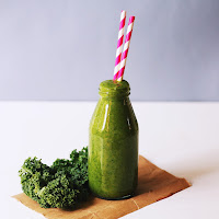 glass bottle holding a green smoothie with a red and white straw
